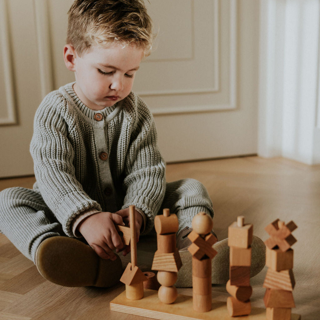 Grijs gehaakt vestje met knopen aan bij jongen die met houten speelgoed speelt