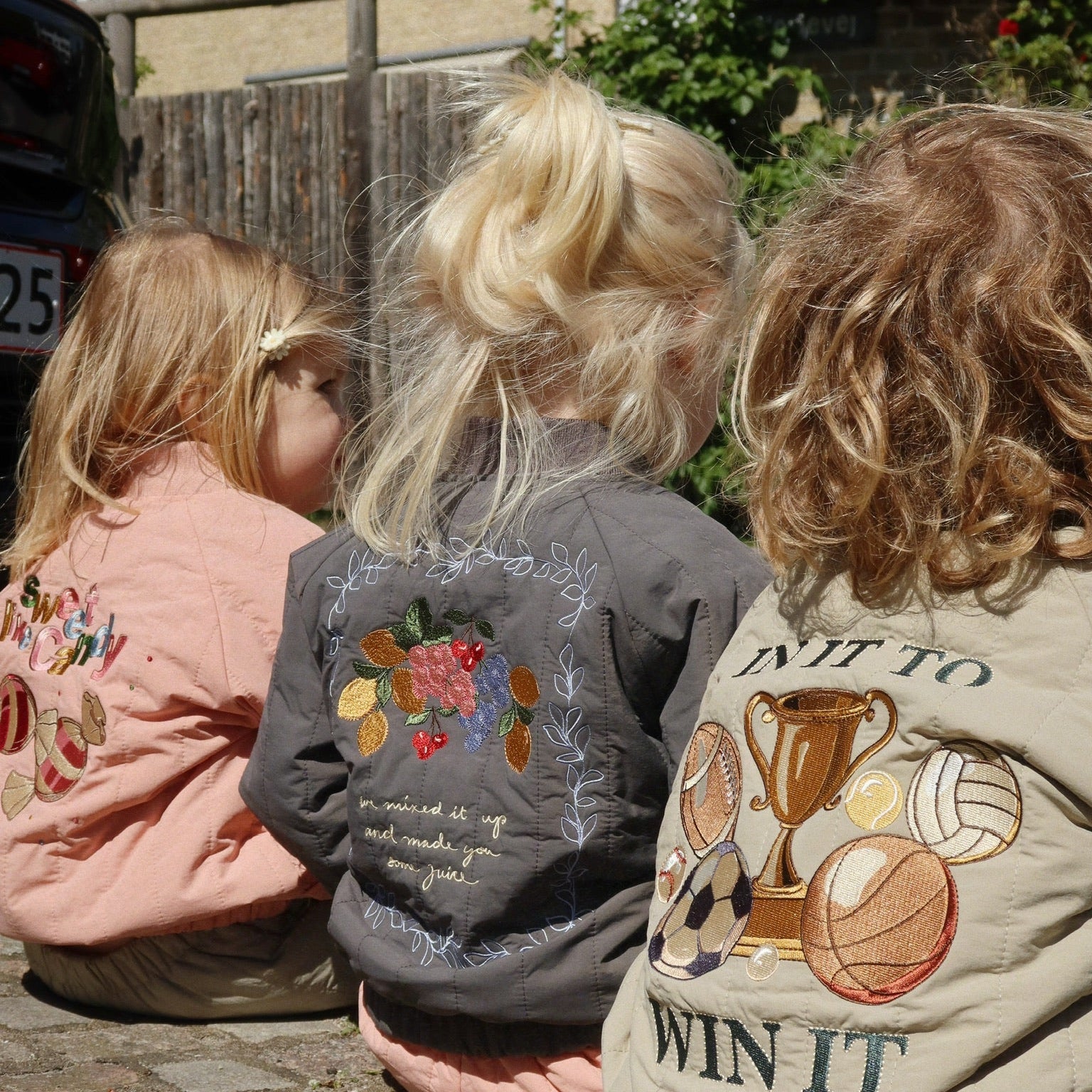 Juno bombers jasjes van Konges Slojd aan bij drie kindjes die op een rijtje zitten, achterkant. 